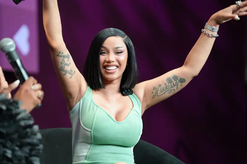 Cardi B smiling with both arms raised on stage during a panel at the 2026 Essence Festival of Culture in New Orleans