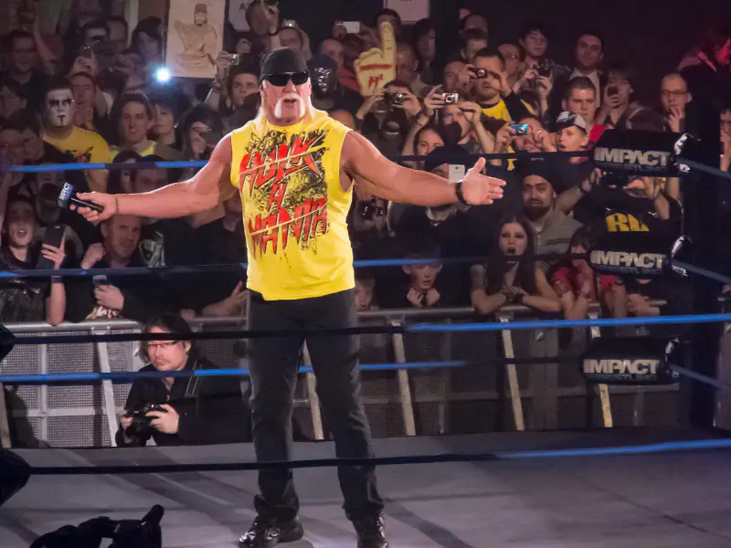 Hulk Hogan in a yellow shirt and black bandana standing in a TNA wrestling ring with fans behind him, January 2013